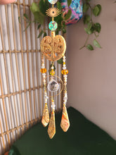 Load image into Gallery viewer, Maori suncatcher with gold elements and beads against a neutral background

